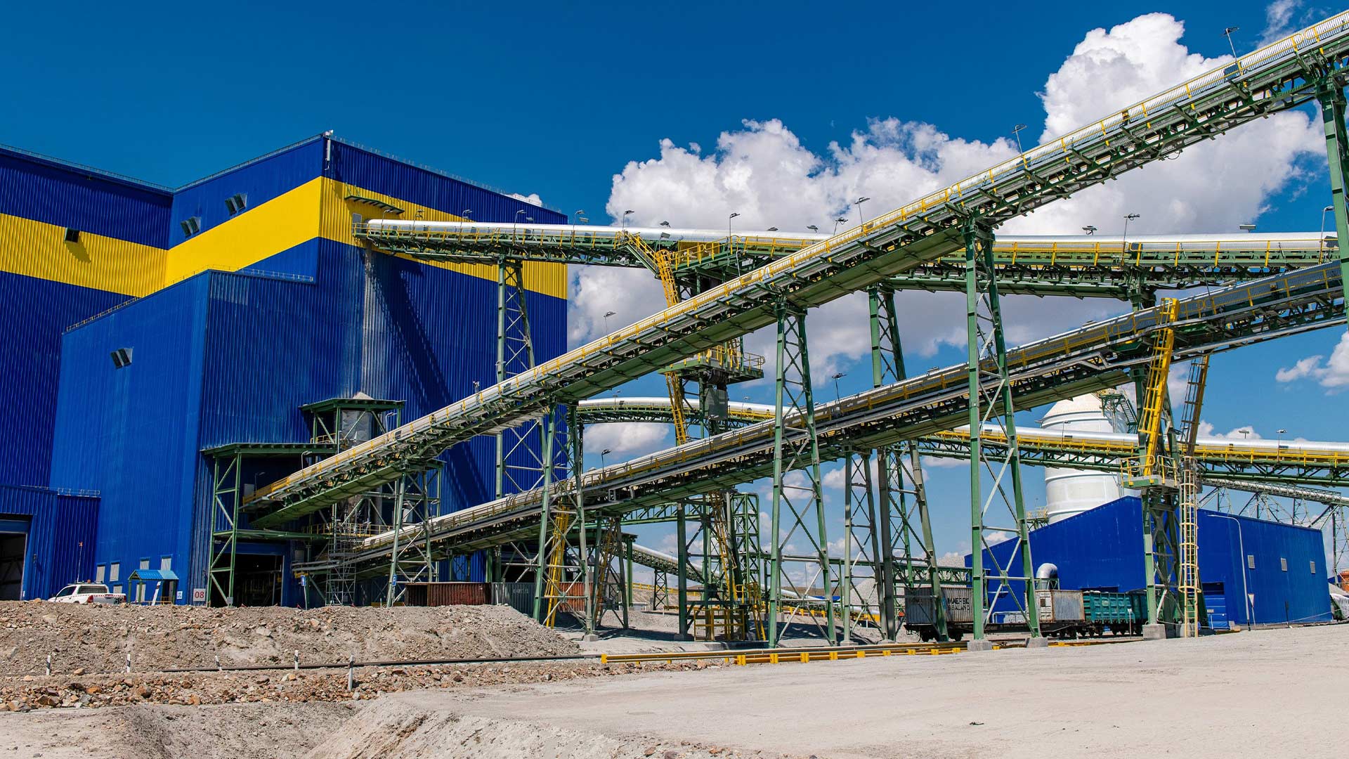 На фотографии — территория горнодобывающего предприятия. Видно, как большие трубы транспортируют материалы в здание.