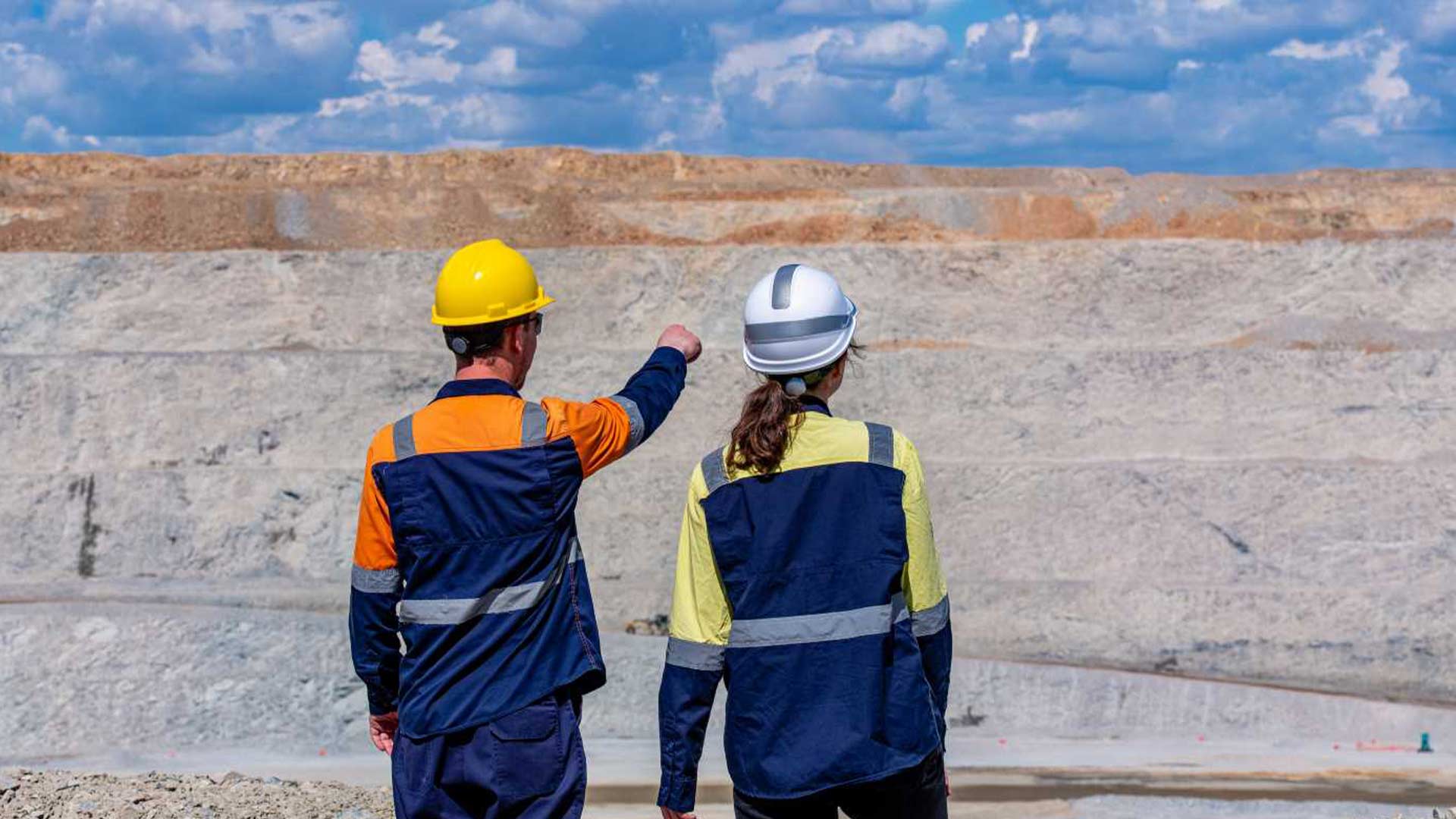 Двое рабочих, снятые со спины, указывают пальцами и смотрят вдаль, в сторону гор.