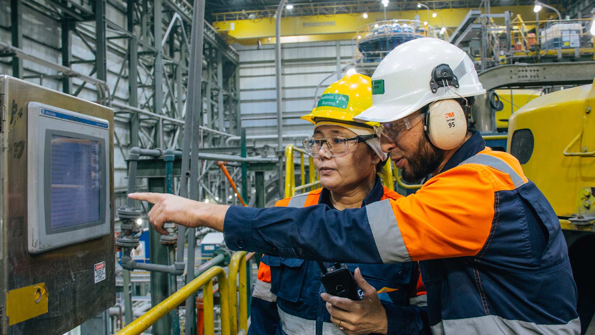 Двое рабочих внутри перерабатывающего цеха используют сенсорный экран.