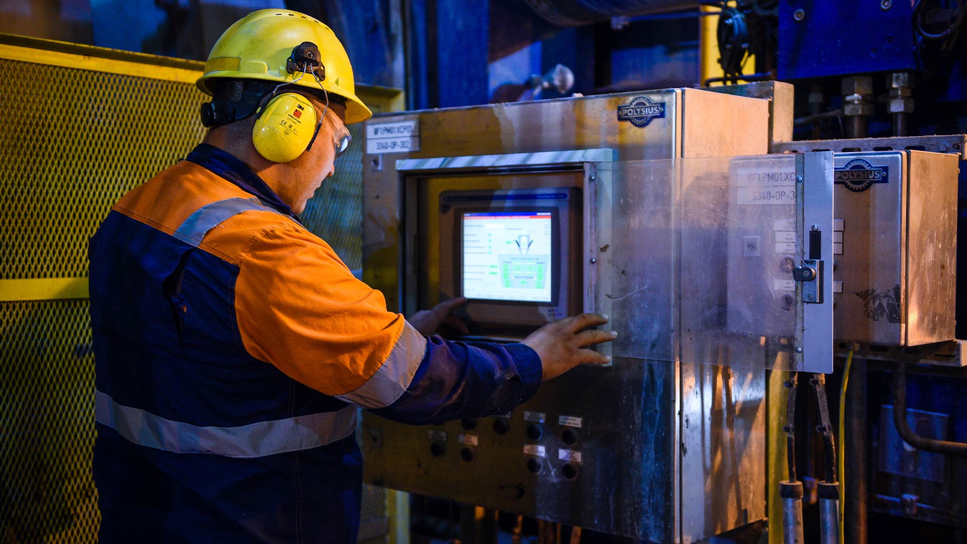 Вид сзади на рабочего Kaz Minerals в защитном шлеме и одежде, смотрящего на небольшой экран.