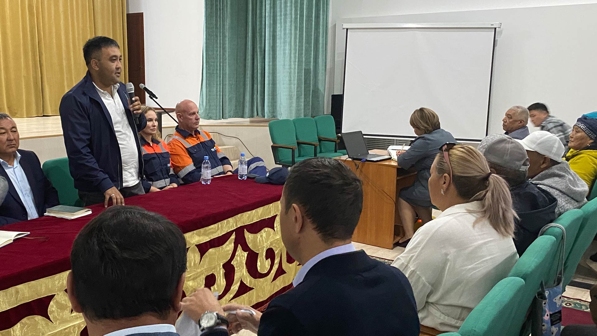 Человек стоит и выступает перед сидящей, заинтересованной аудиторией.