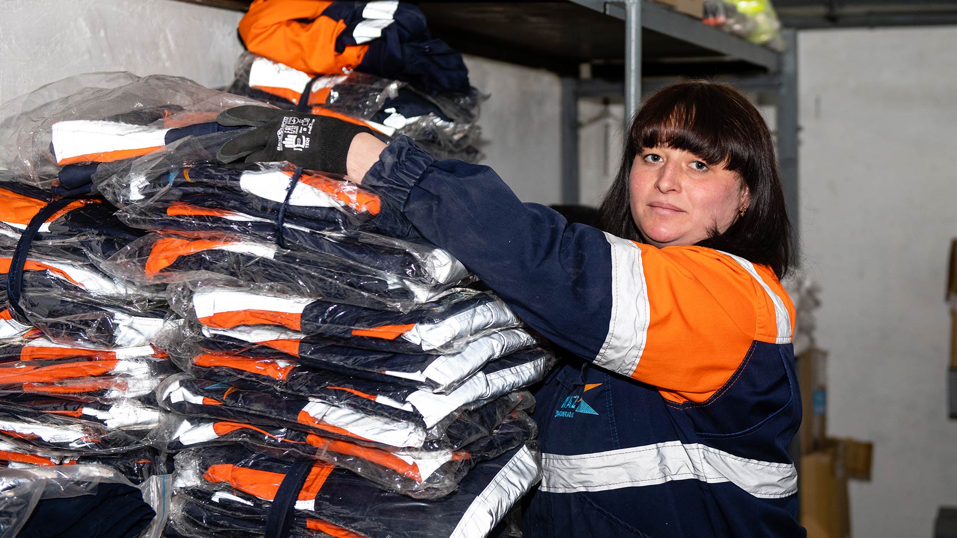 Человек в защитной экипировке смотрит в камеру. На заднем плане видна техника.